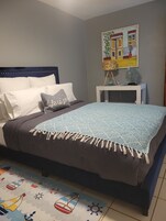 Quarto com cama, travesseiros, mesa de cabeceira, abajur e pintura na parede.