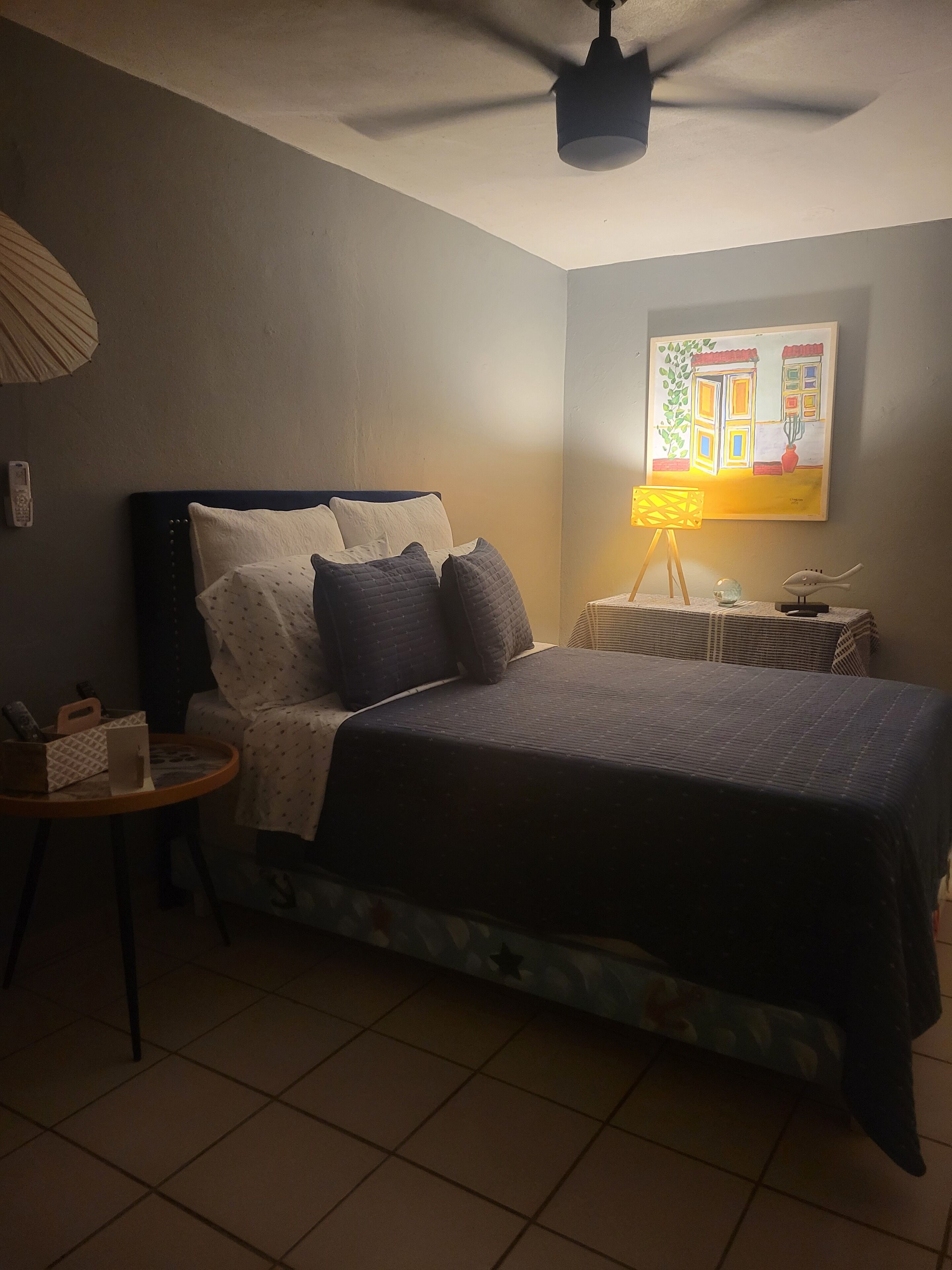 Een slaapkamer met een bed, nachtkastje, lamp en plafondventilator.