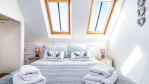 Une chambre à coucher comprenant un lit, deux tables de chevet, une commode et deux fenêtres de toit.