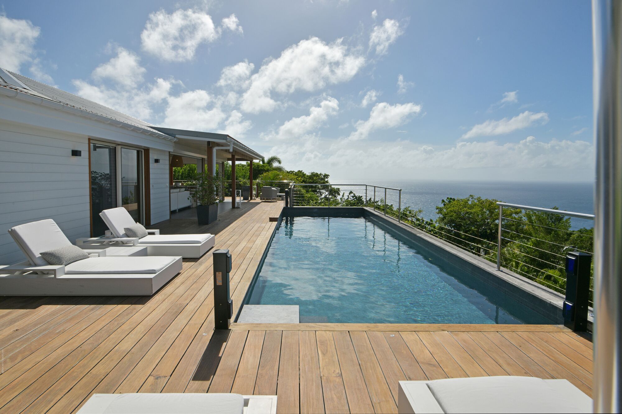 A poolside area with lounge chairs, a wooden deck, and a view of the ocean.