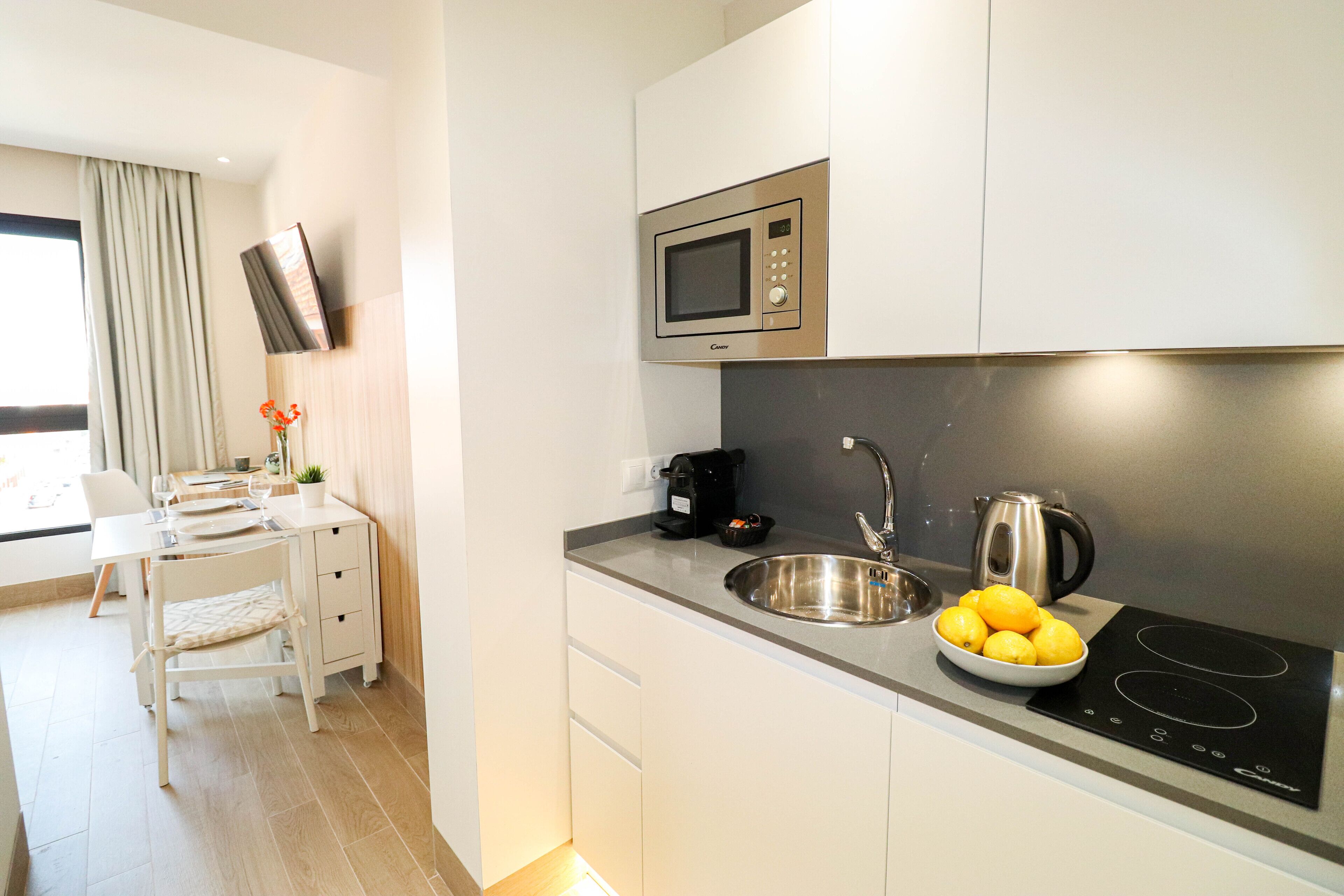 A modern kitchen with a built-in microwave, sink, and induction cooktop. There is a bowl of lemons on the counter.