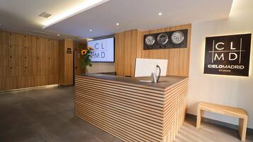 A reception area with a wooden reception desk, a TV screen displaying 'CLMD', and a sign for 'Cielomadrid Studios'.
