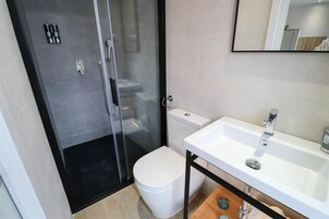 Ein modernes Badezimmer mit einer Duschkabine aus Glas, einer weißen Toilette und einem weißen Waschbecken mit chromfarbenen Armatur.