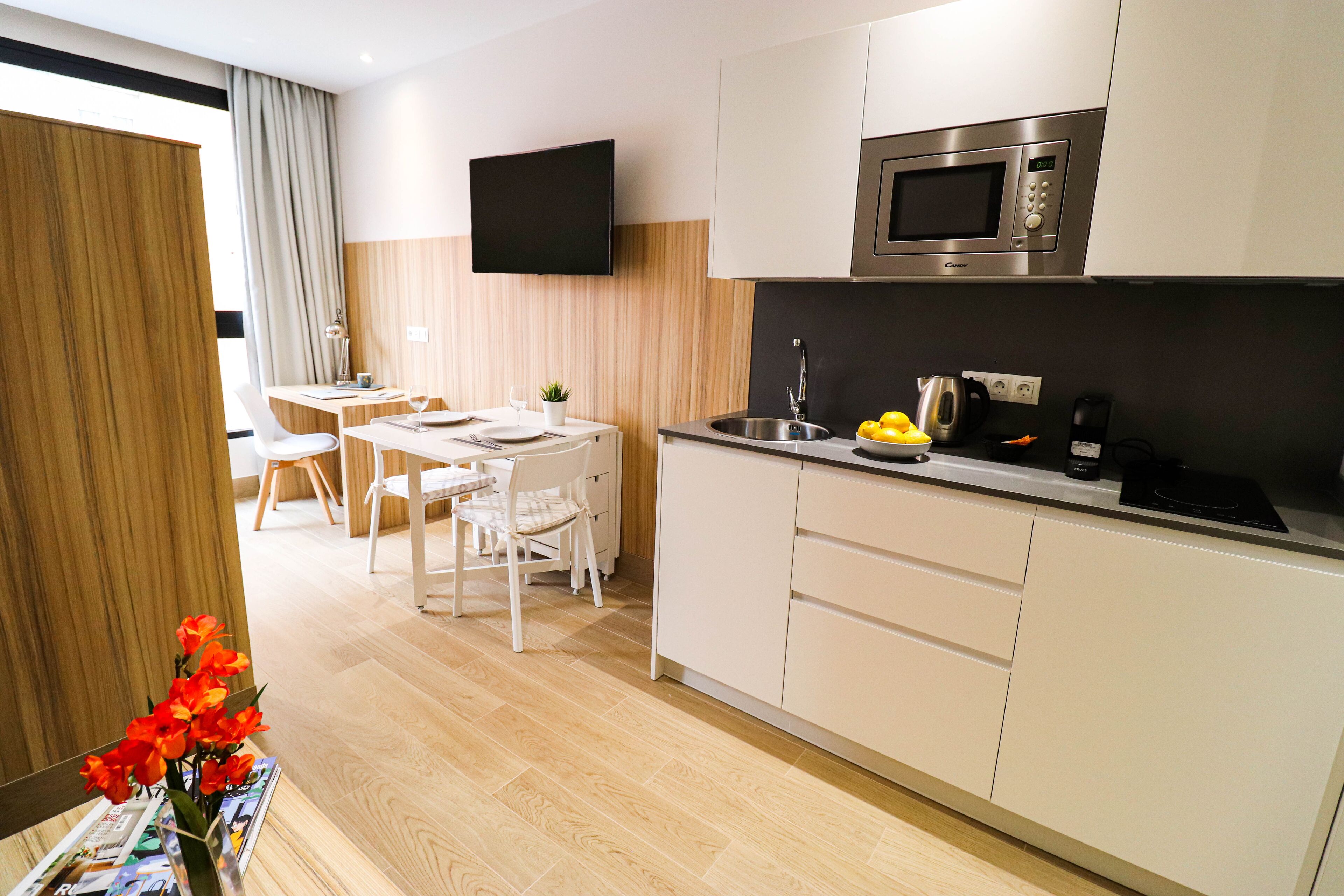 A modern kitchen with white cabinets, a stainless steel microwave, and a dining area with a white table and chairs.