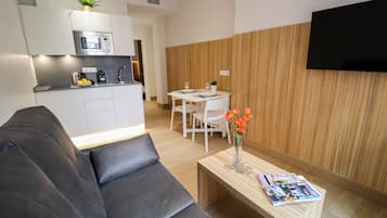 Una sala de estar moderna con un sofá gris, una mesa de centro de madera con revistas, y un comedor con una mesa y sillas blancas.