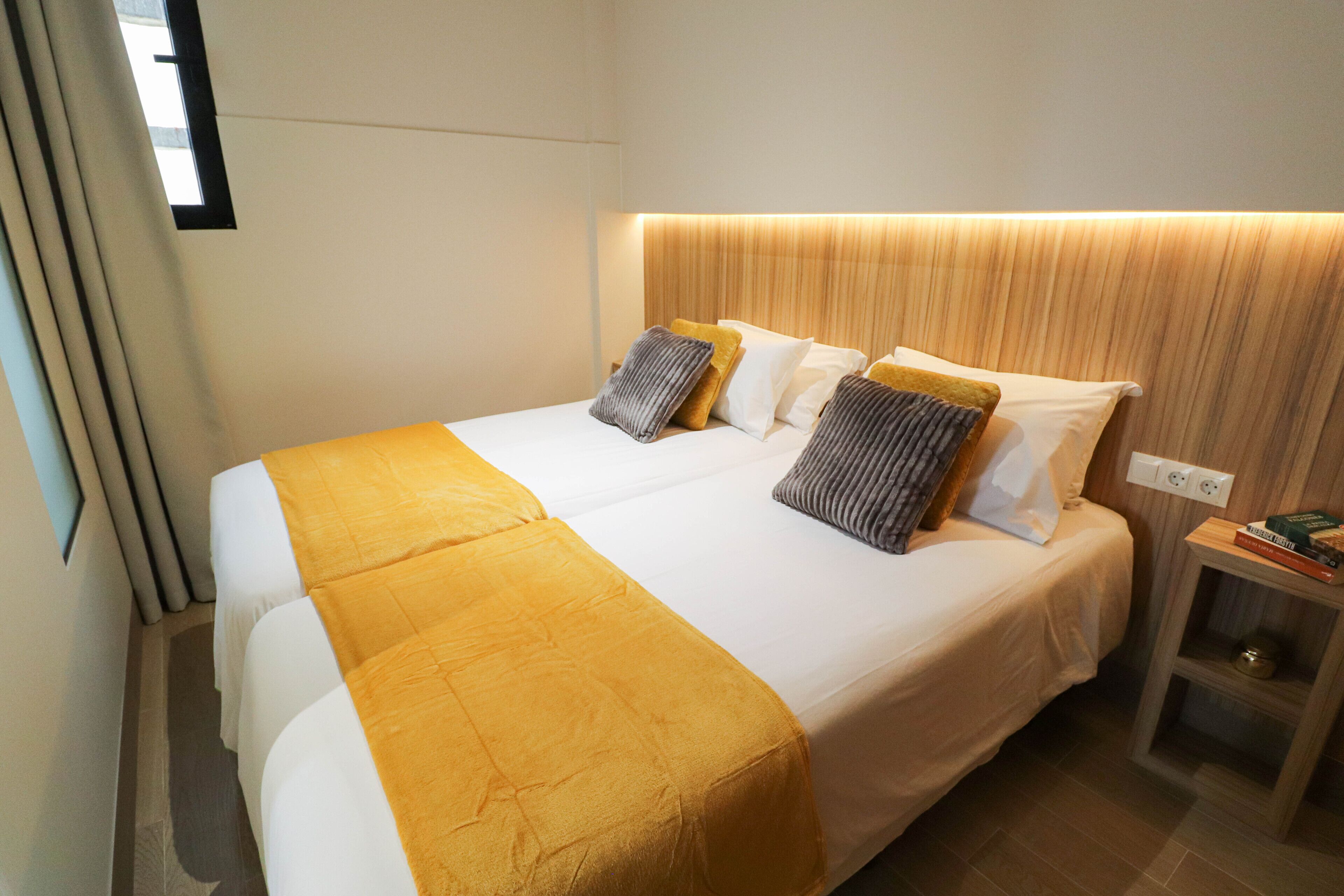 A hotel room with a large bed, two pillows, a bedside table, and a nightstand.