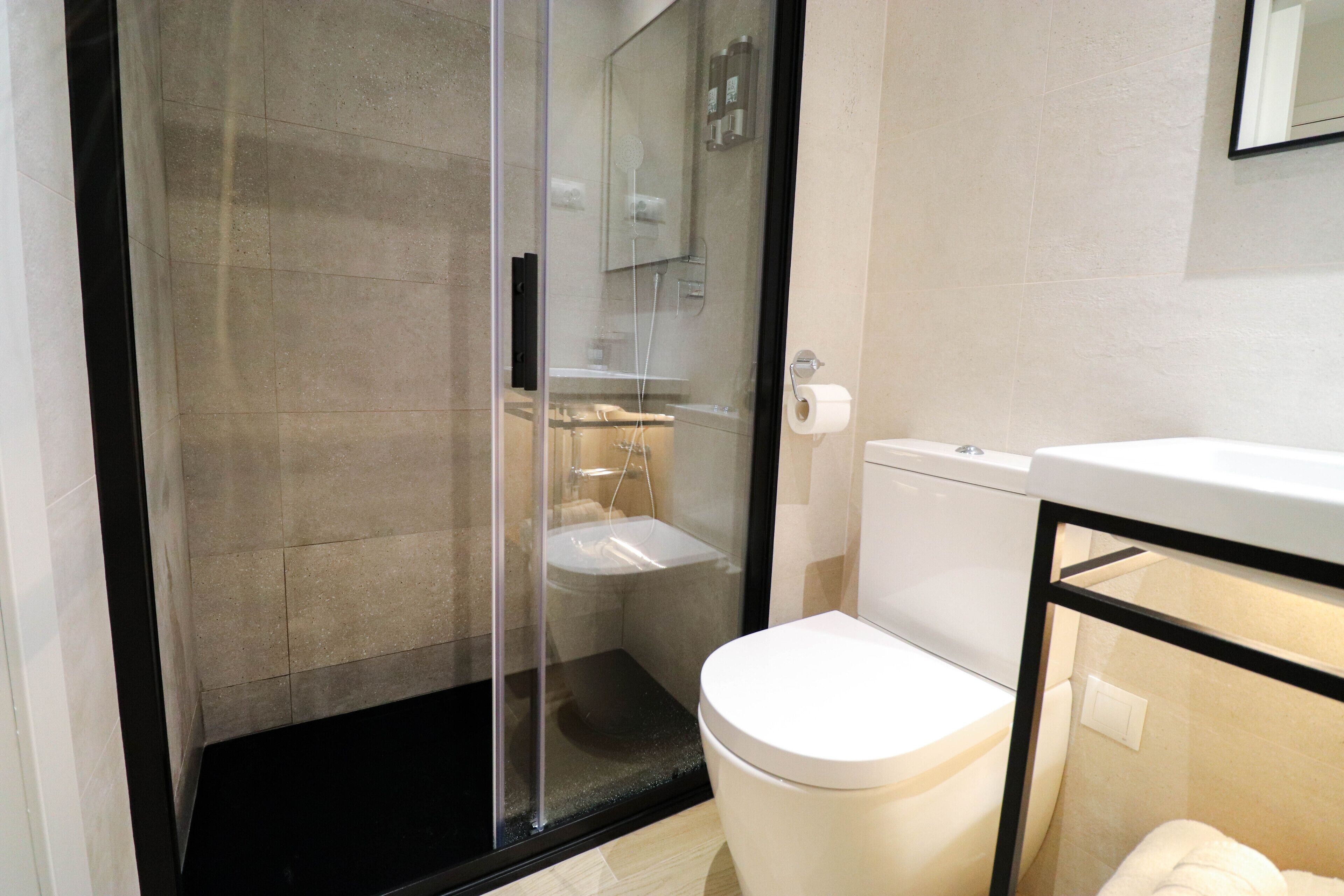 Un baño moderno con ducha de vidrio, inodoro blanco y lavamanos.