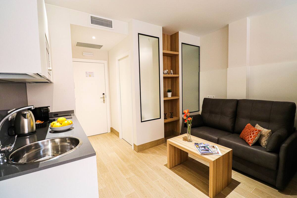 Una cocina moderna con un lavamanos, hervidor y limones, una mesa de centro de madera y un sofá de cuero negro.
