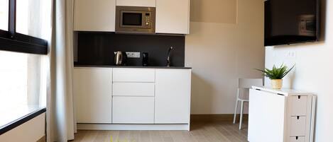 A modern kitchen with white cabinetry, a microwave, a kettle, and a small table with a plant.