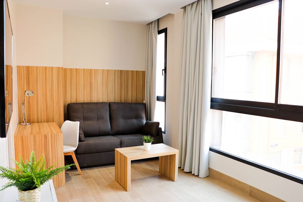 Una sala moderna con un sofá oscuro, una mesa de centro de madera y una lámpara.