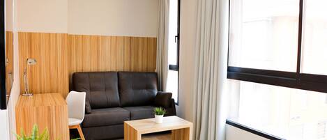 Una sala moderna con un sofá oscuro, una mesa de centro de madera y una lámpara.