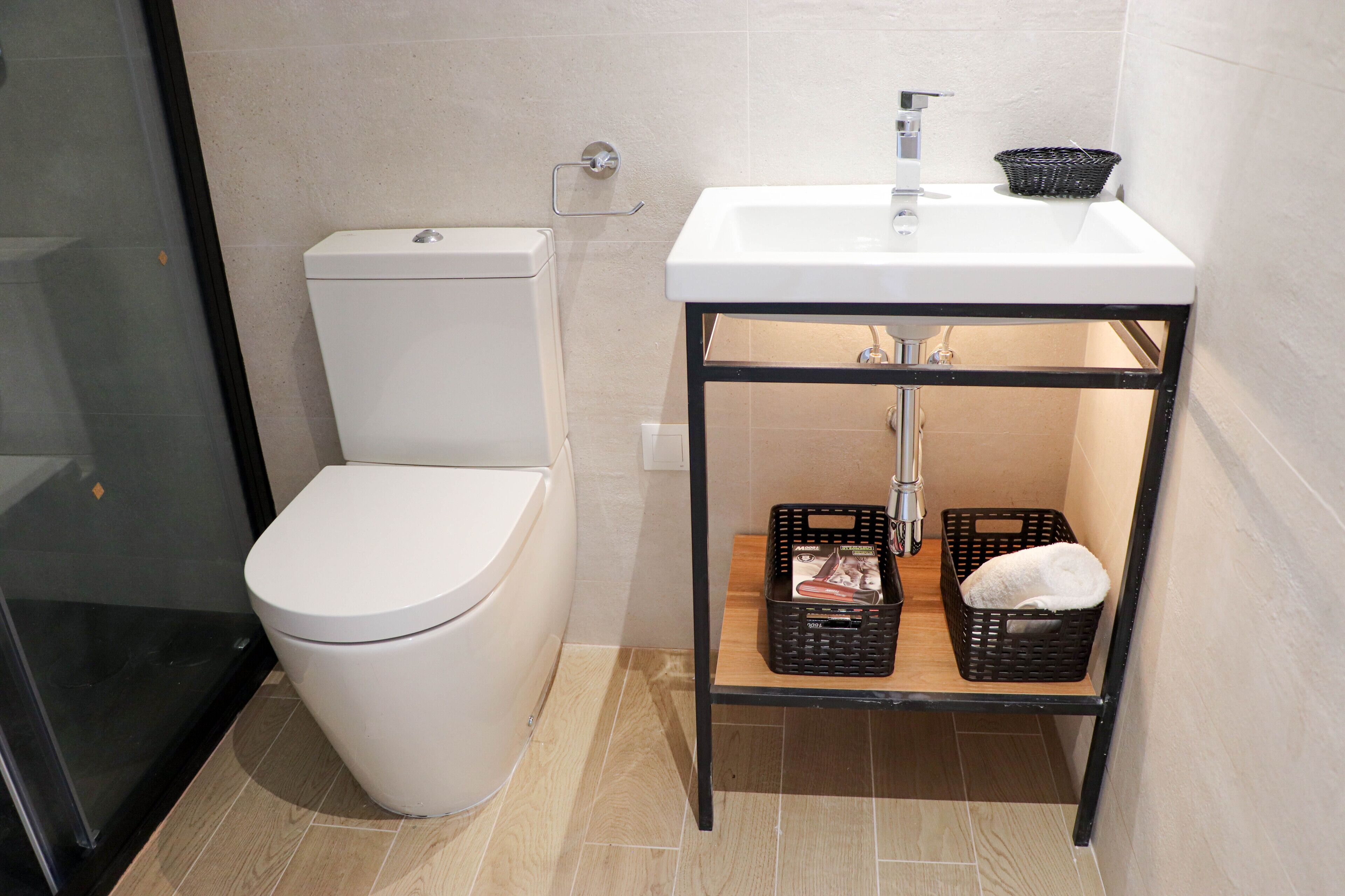 Een badkamer met een wit toilet, een wastafel met een zwart frame, en twee manden op een plank.