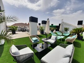 Eine Dachterrasse mit Gartenmöbeln, darunter Korbstühle und ein Tisch, umgeben von Kunstrasen und Topfpflanzen.