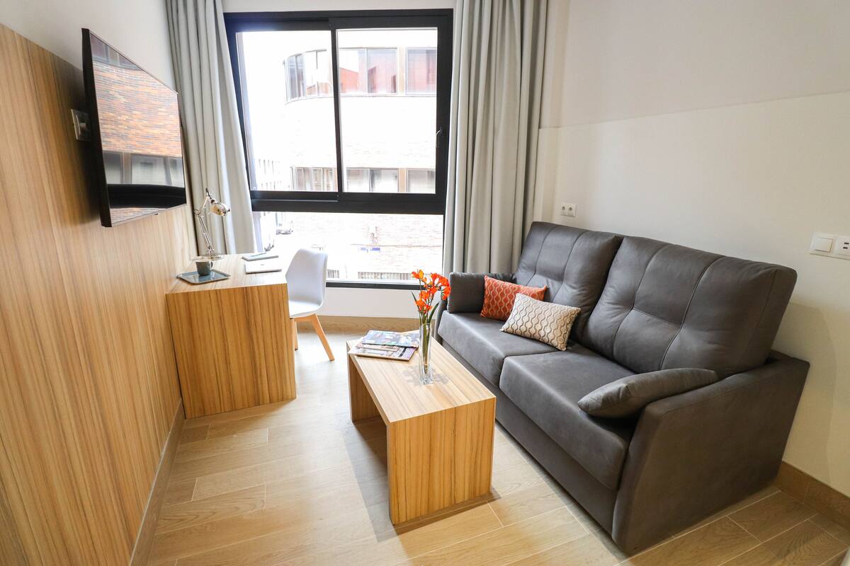 Una sala de estar moderna con un sofá gris, una mesa de centro de madera y un televisor de pantalla plana montado en la pared.