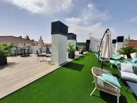Een terras op het dak met kunstgras, tuinmeubels en planten in potten.