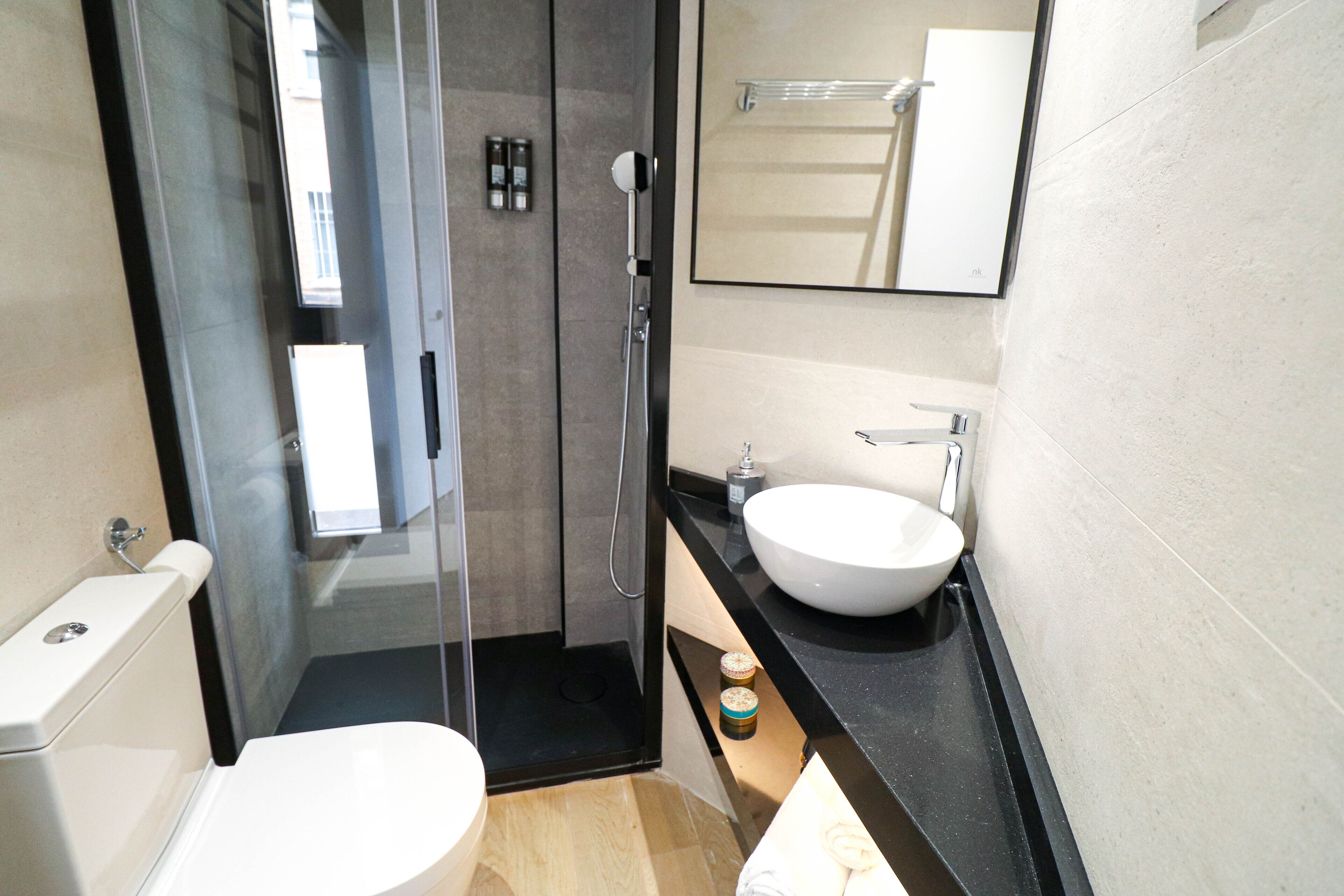 Et moderne badeværelse med en glasafskærmet bruseniche, et hvidt håndvaskarrangement og et toilet.
