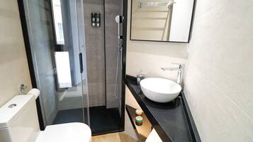Et moderne badeværelse med en glasafskærmet bruseniche, et hvidt håndvaskarrangement og et toilet.