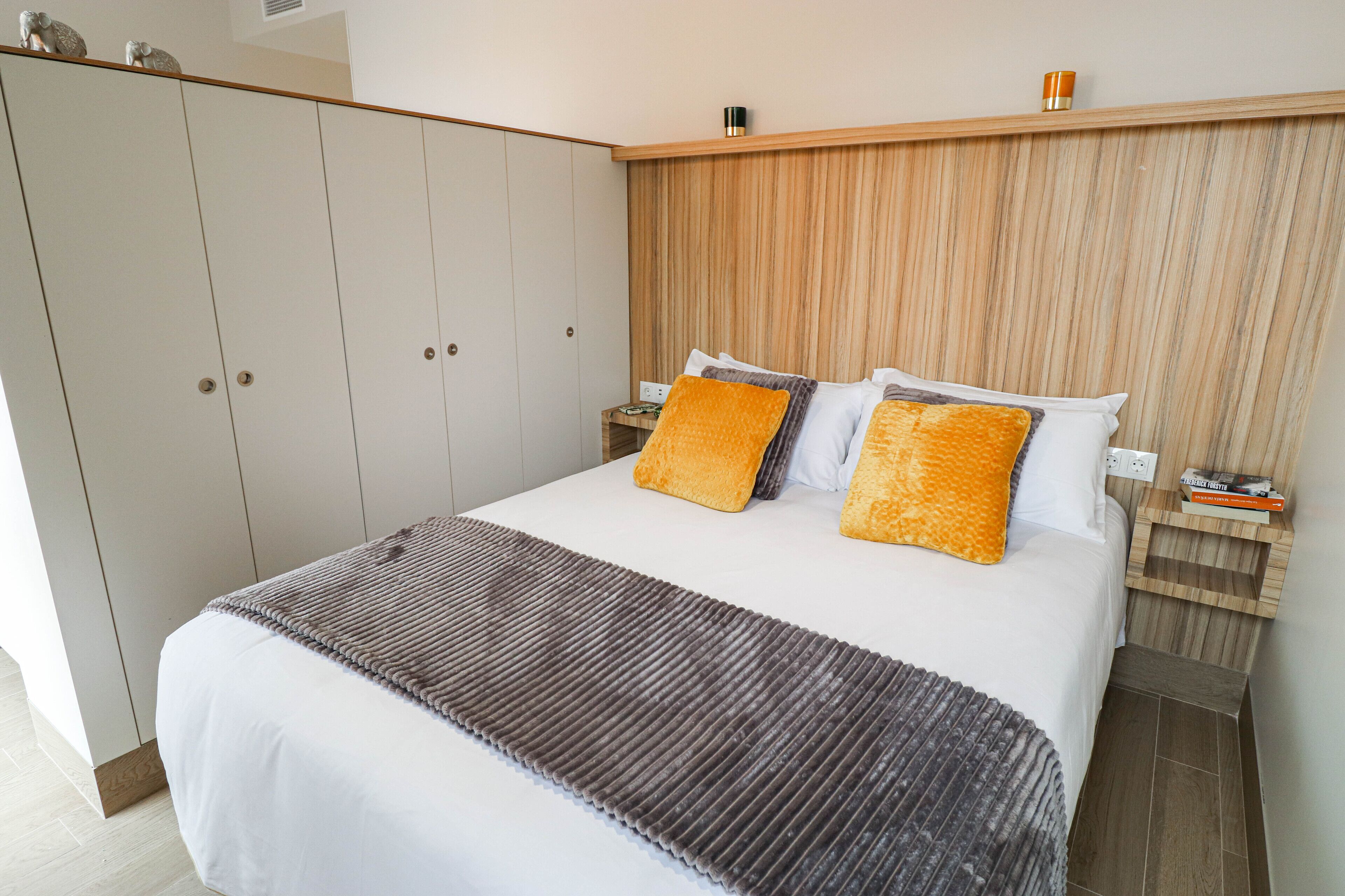 A bedroom with a large bed, wooden headboard, two nightstands, and a wardrobe.