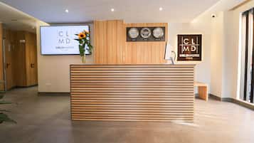 Una recepción con diseño de listones de madera, un jarrón con flores y dos pantallas digitales grandes con la marca 'CLMD CIELOMADRID STUDIO'.
