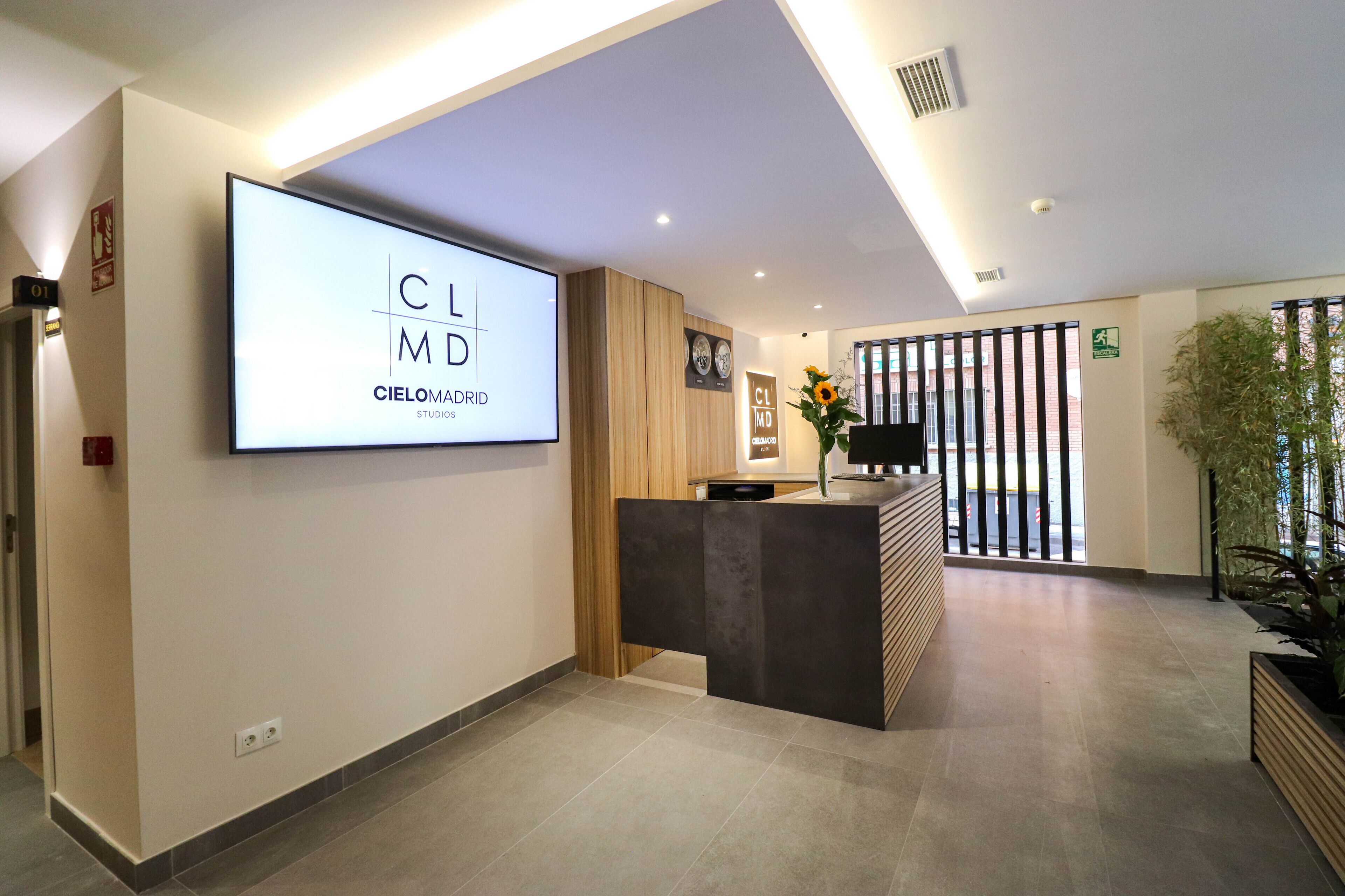A modern reception area with a large screen displaying 'Cielomadrid Studios' and a reception desk.