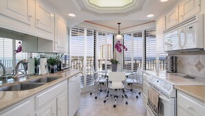 A modern kitchen with white cabinetry, a central island with seating, a built-in oven, and a view through large windows. - Wake up to beautiful ocean views!!! (MYRTLE BEACH)