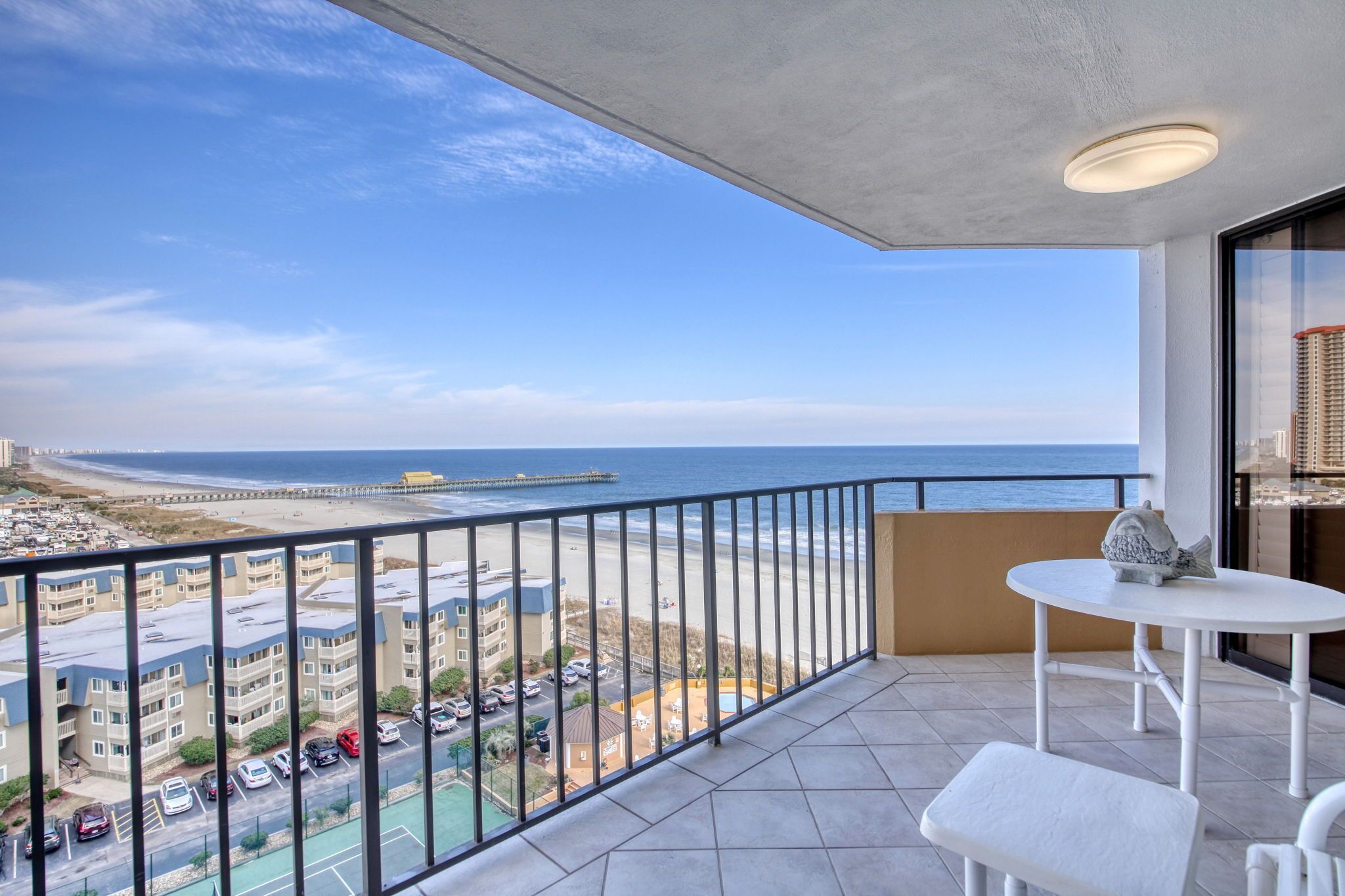 A balcony with a view of the beach and ocean, a white table, and a white chair.