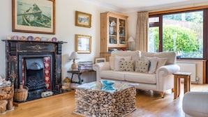 A living room with a fireplace, a sofa, a glass coffee table, and a view of greenery outside.