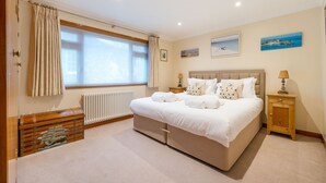 A bedroom with a large bed, a wooden chest, a radiator, and a window with curtains.
