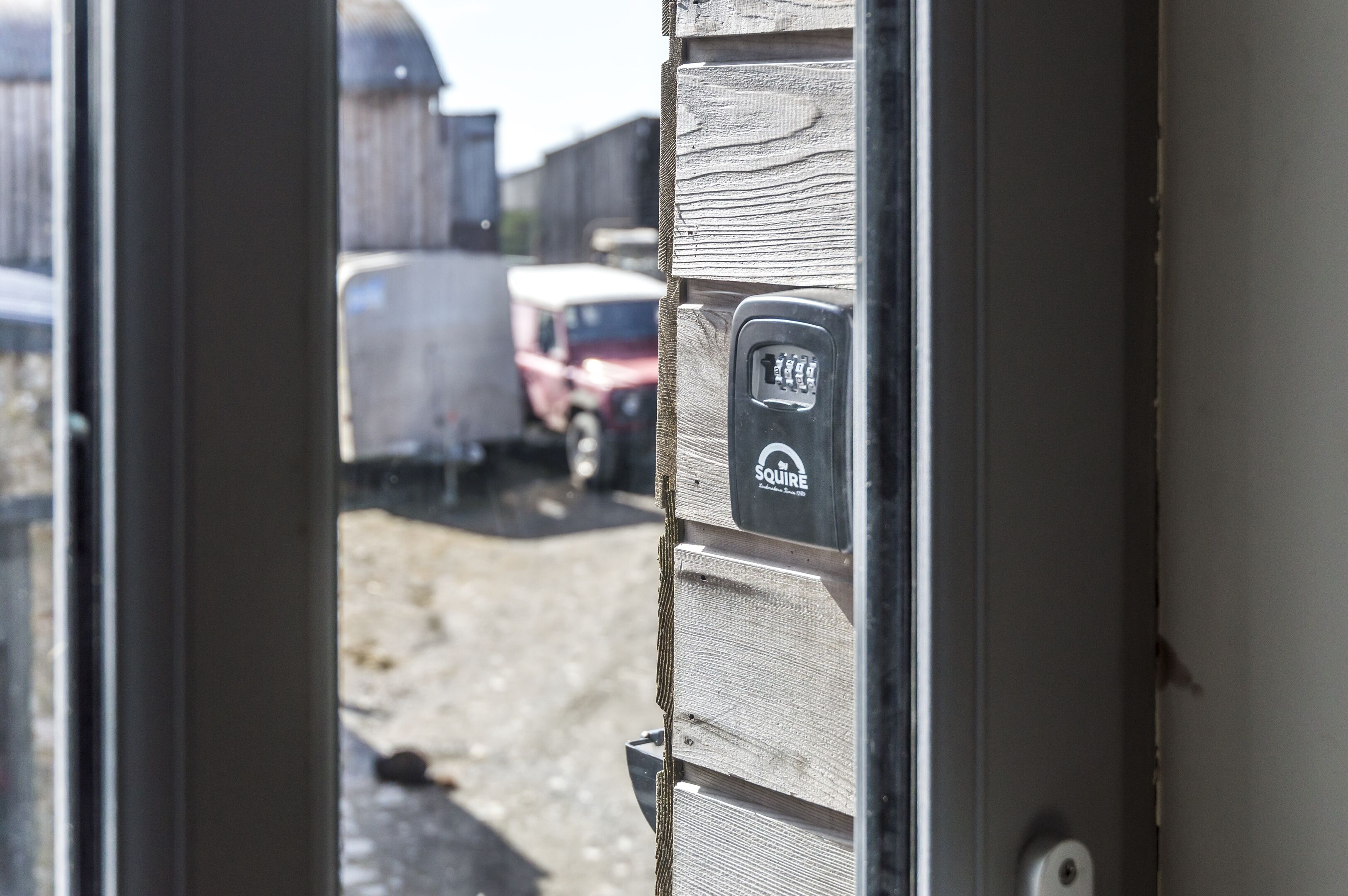 A door with a security keypad and a view of a parking area with vehicles.