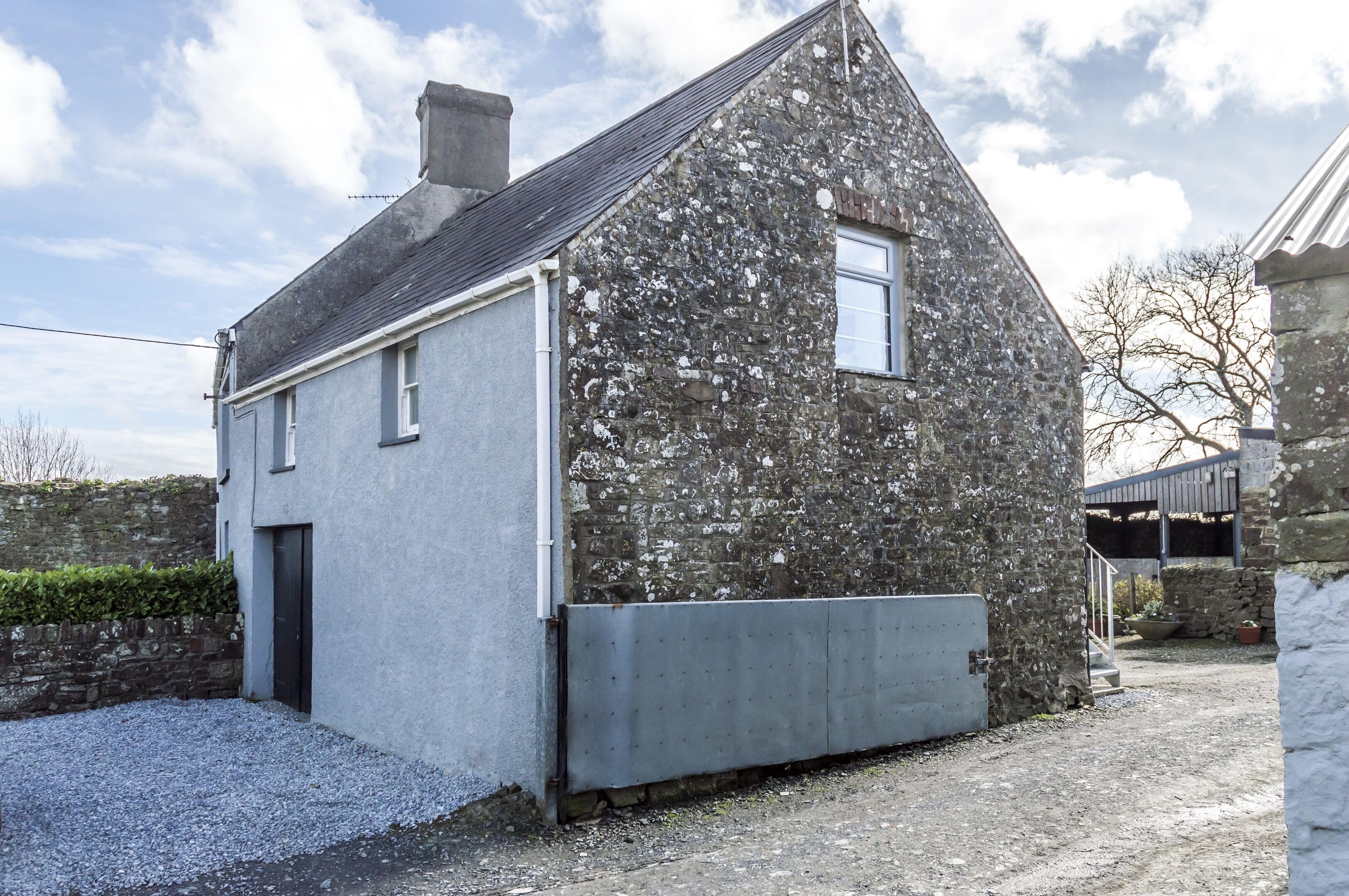 Une maison en pierre à l’extérieur gris, avec une petite fenêtre et une porte.