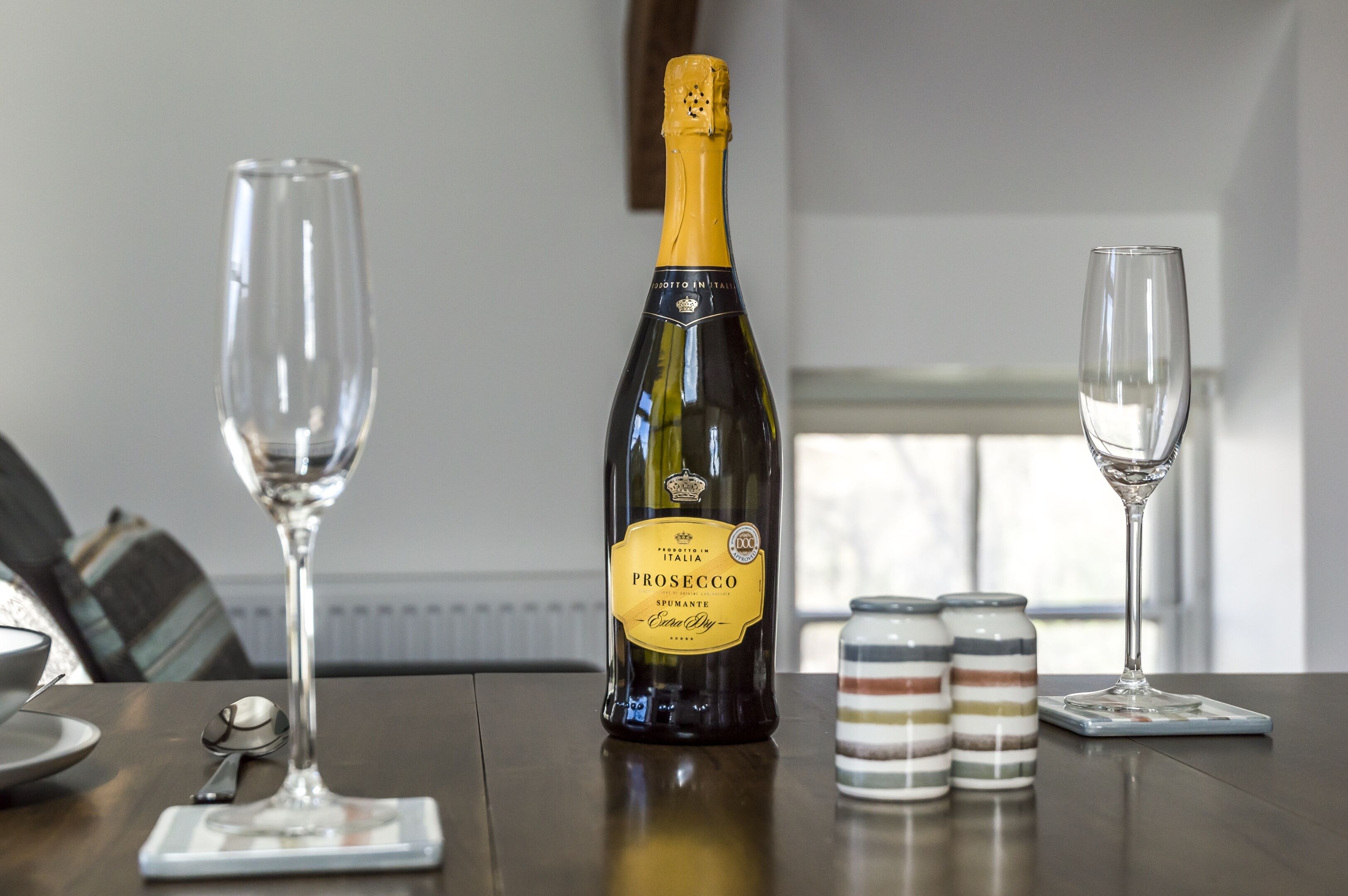 Eine Prosecco-Flasche auf einem Tisch mit zwei Weingläsern und einem Löffel.