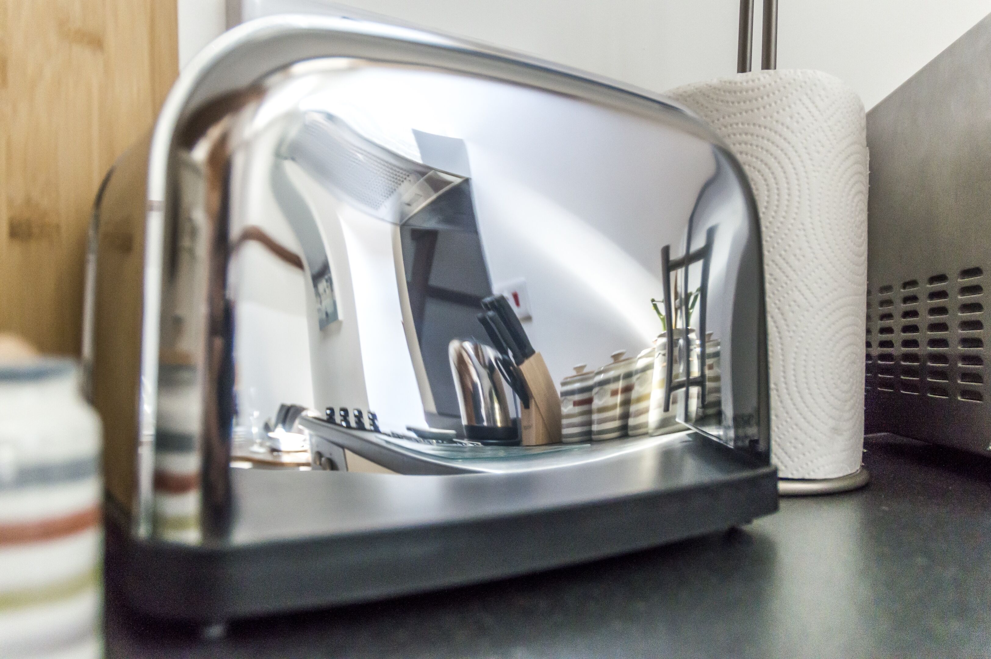 En rustfrit stål-toaster med reflekterende overflade, en rulle hvide køkkenrulle og en metalventil på en køkkenbordplade.