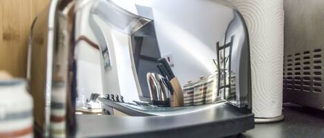 En rustfrit stål-toaster med reflekterende overflade, en rulle hvide køkkenrulle og en metalventil på en køkkenbordplade.