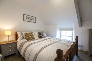 Un dormitorio con una cama de madera, una mesita de noche con cajones, una lámpara de noche y una ventana con vistas al exterior.