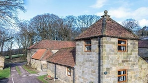 A stone building with a tiled roof, a small garden, and a paved driveway.