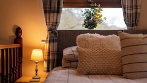 A bedroom with a bed, a nightstand with a lamp, plaid curtains, and a window with a view of greenery.