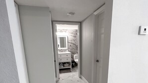 Un pasillo con piso de mármol que conduce a un baño con salpicadero de mármol y un lavamanos blanco.