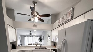 Una cocina moderna con armarios blancos, horno empotrado, refrigerador y ventilador de techo.