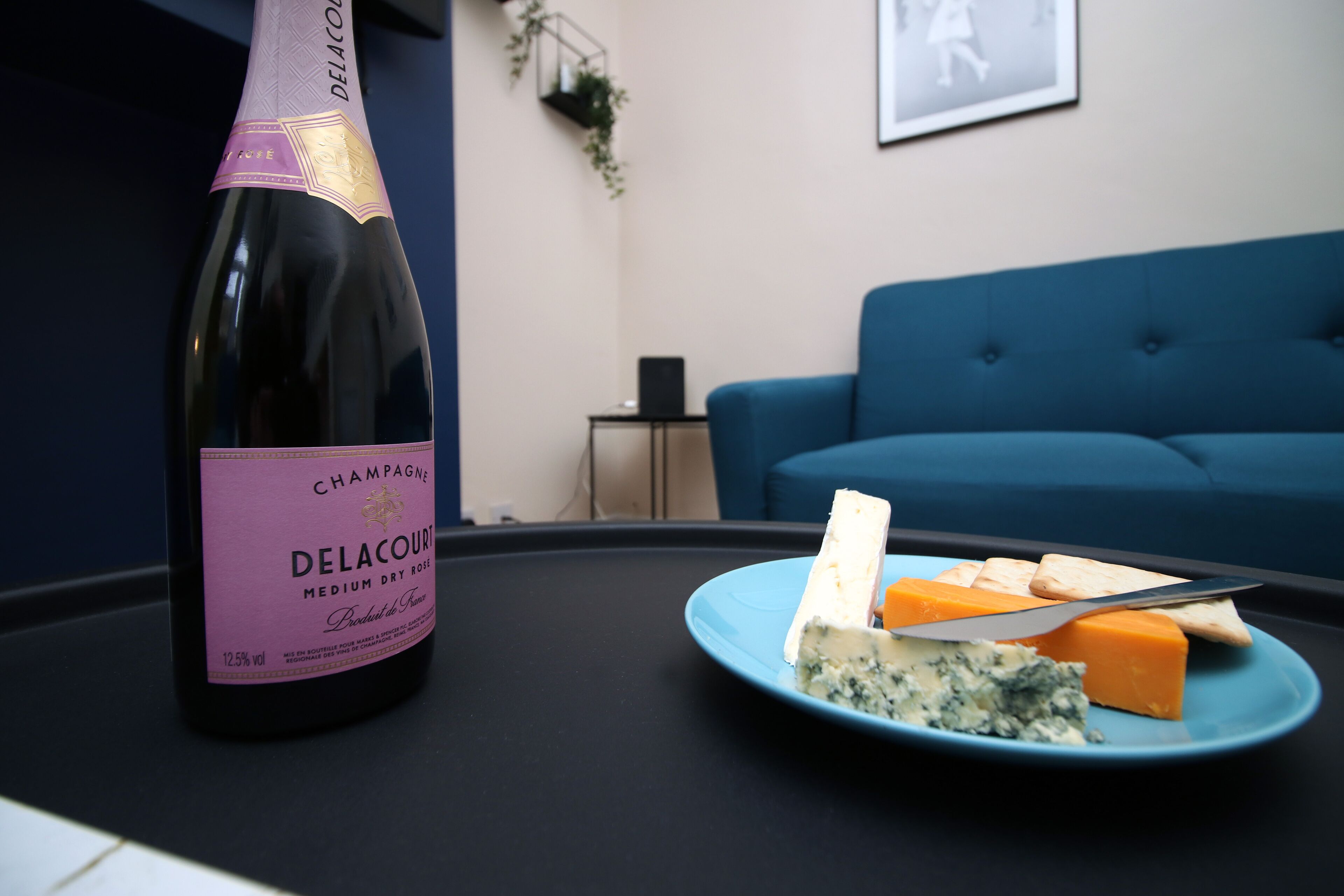 A bottle of Delacour Champagne on a table with a plate of cheese and crackers.
