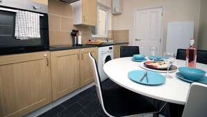 A modern kitchen with wooden cabinets, a built-in oven, a washing machine, and a dining area with blue plates and chairs. - Karah Suites - Church Road I (Bristol)