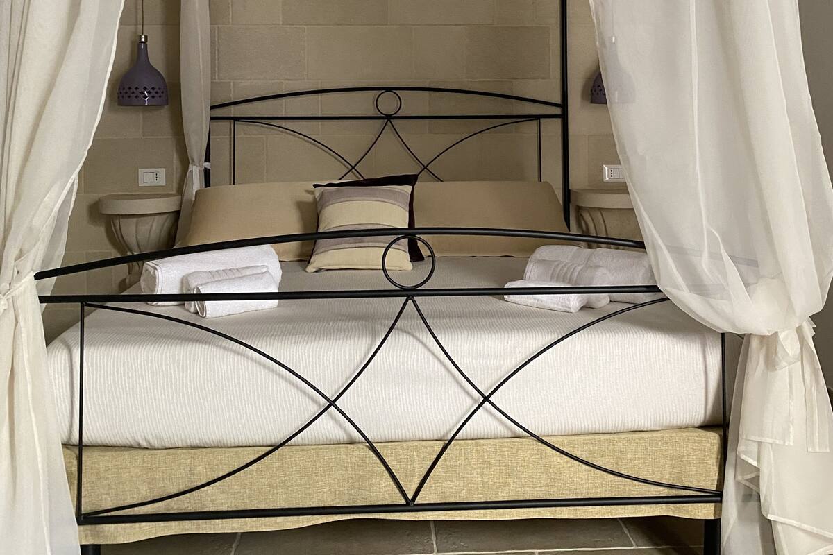 A four-poster bed with a canopy, a bedside table, and a wall-mounted lamp.