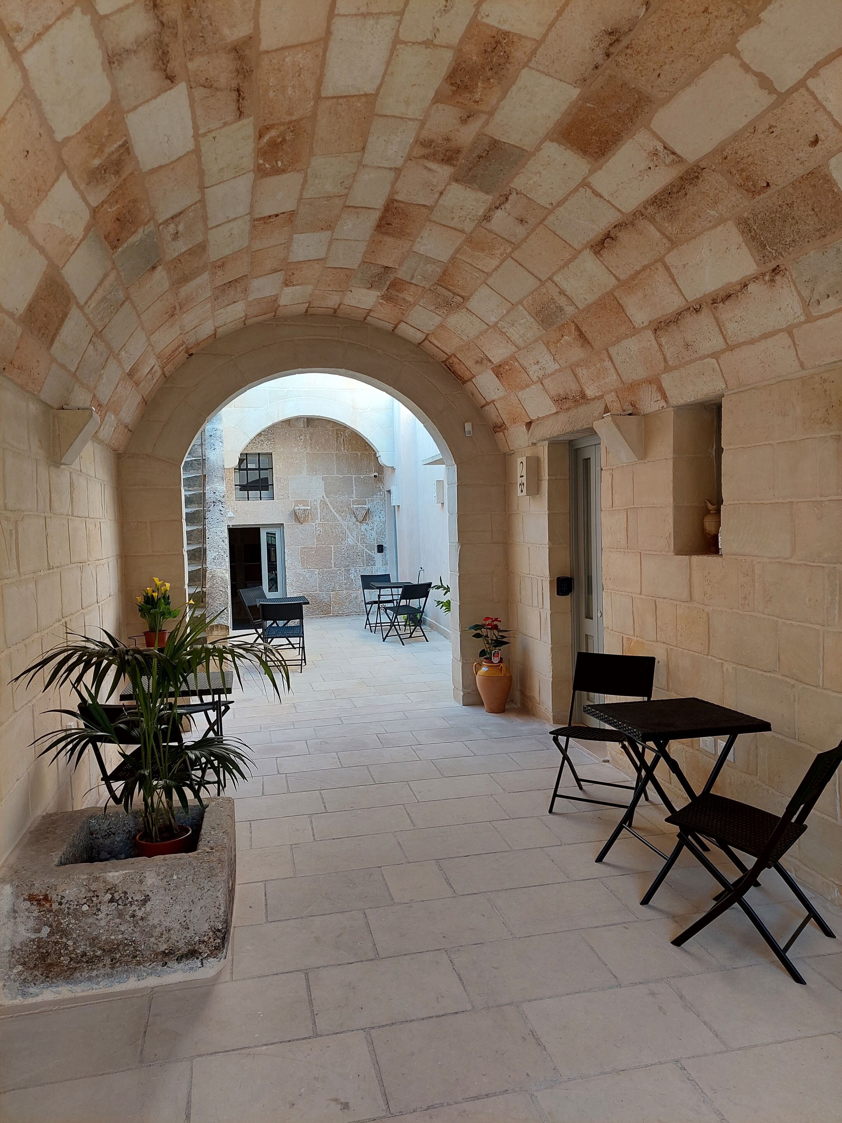Un corridoio ad arco con pavimento piastrellato che conduce a una zona esterna con tavoli e sedie.