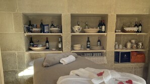 A room with a bed, towels, and shelves with wine bottles and kitchenware. - Dimora Assuntina Fine Rooms (Martano)