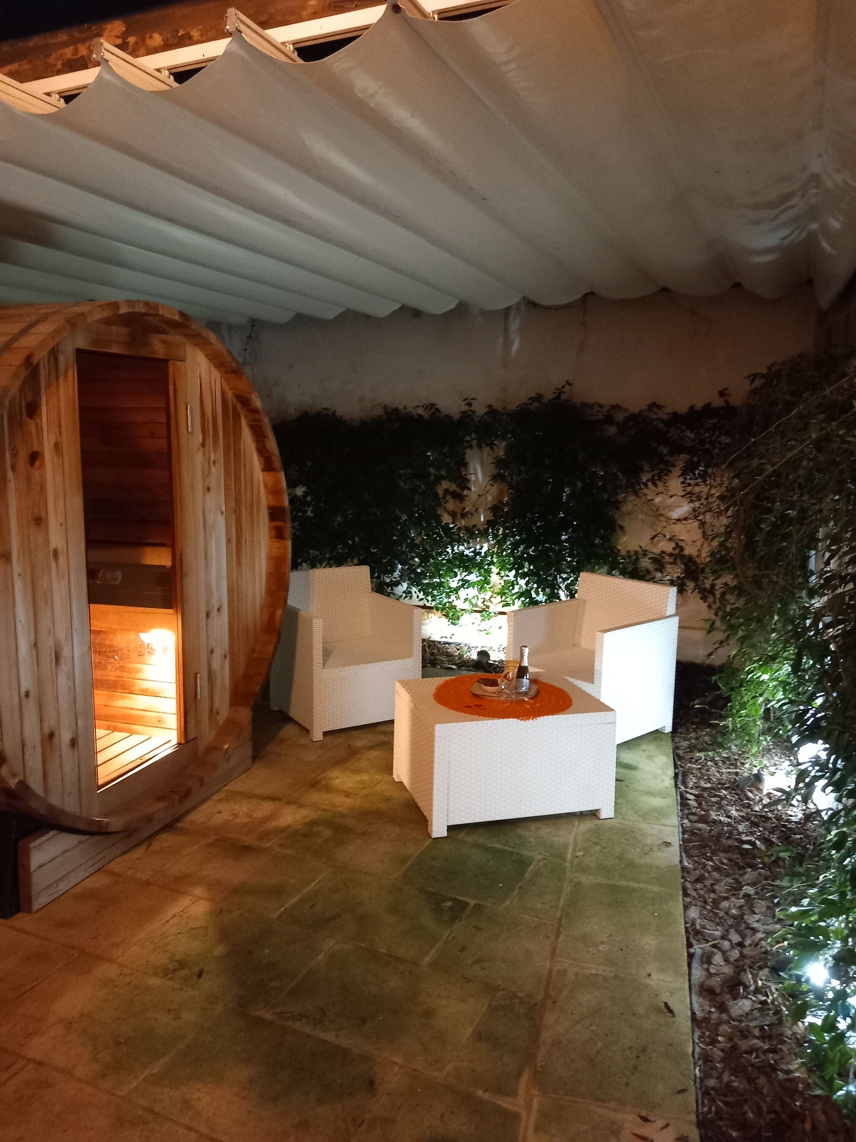 Eine Holzsauna mit weißem Innenraum, ein weißer Außenbereich mit Tisch und eine überdachte Terrasse mit Grünpflanzen.