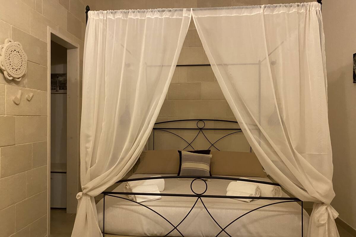 A bed with a metal frame and white canopy, a wall clock, and a door leading to a bathroom.