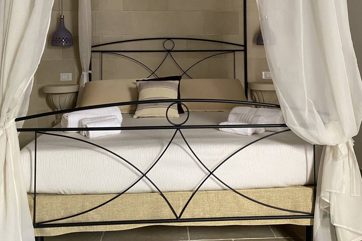 A four-poster bed with a metal frame, white bedding, and sheer curtains.