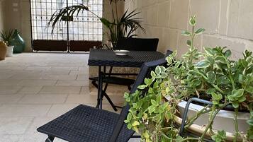 An outdoor patio area with a table and chairs, potted plants, and a large arched window.