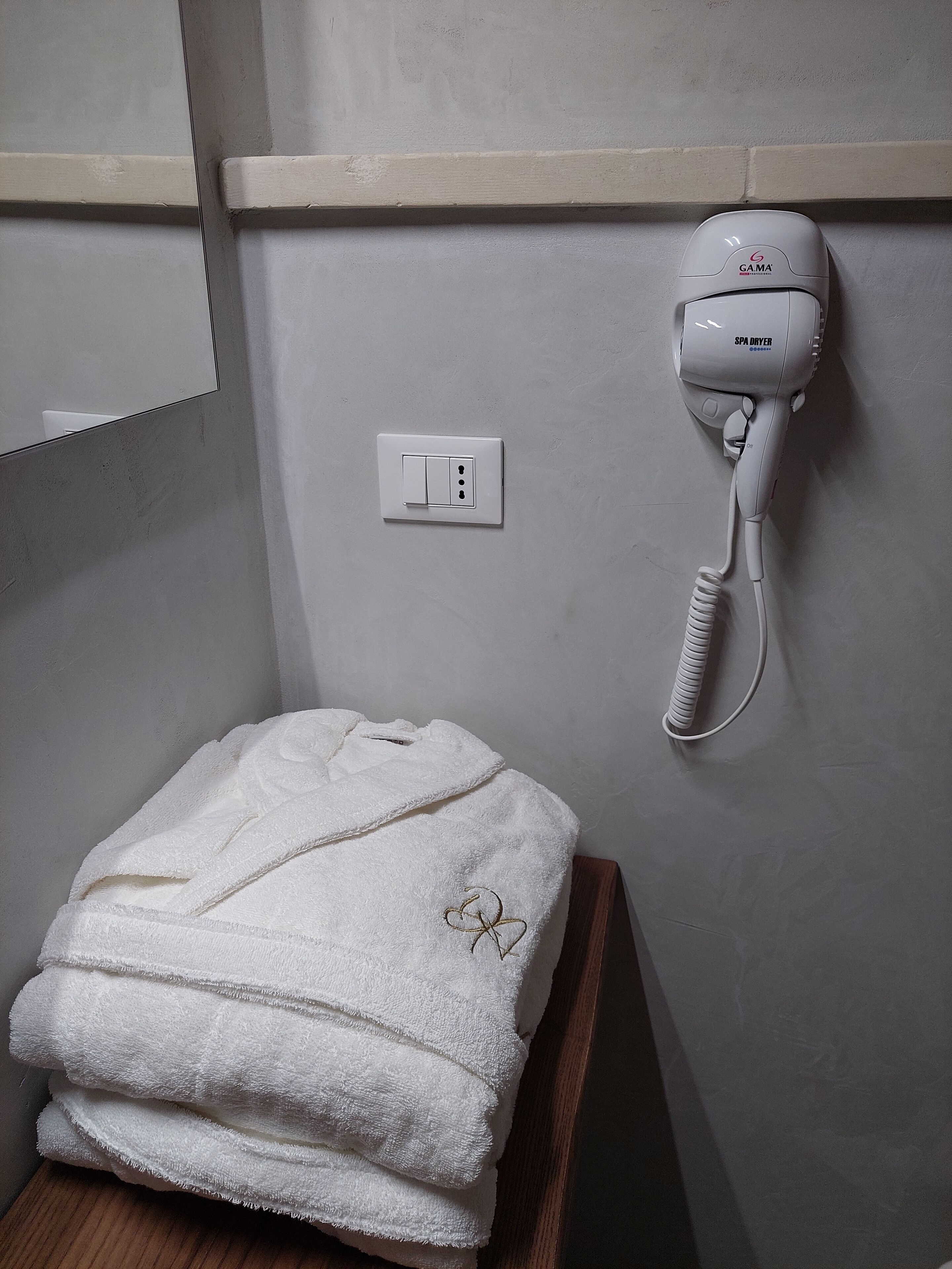 A bathroom with a white towel stack on a wooden stool, a wall-mounted hairdryer, and a light switch.