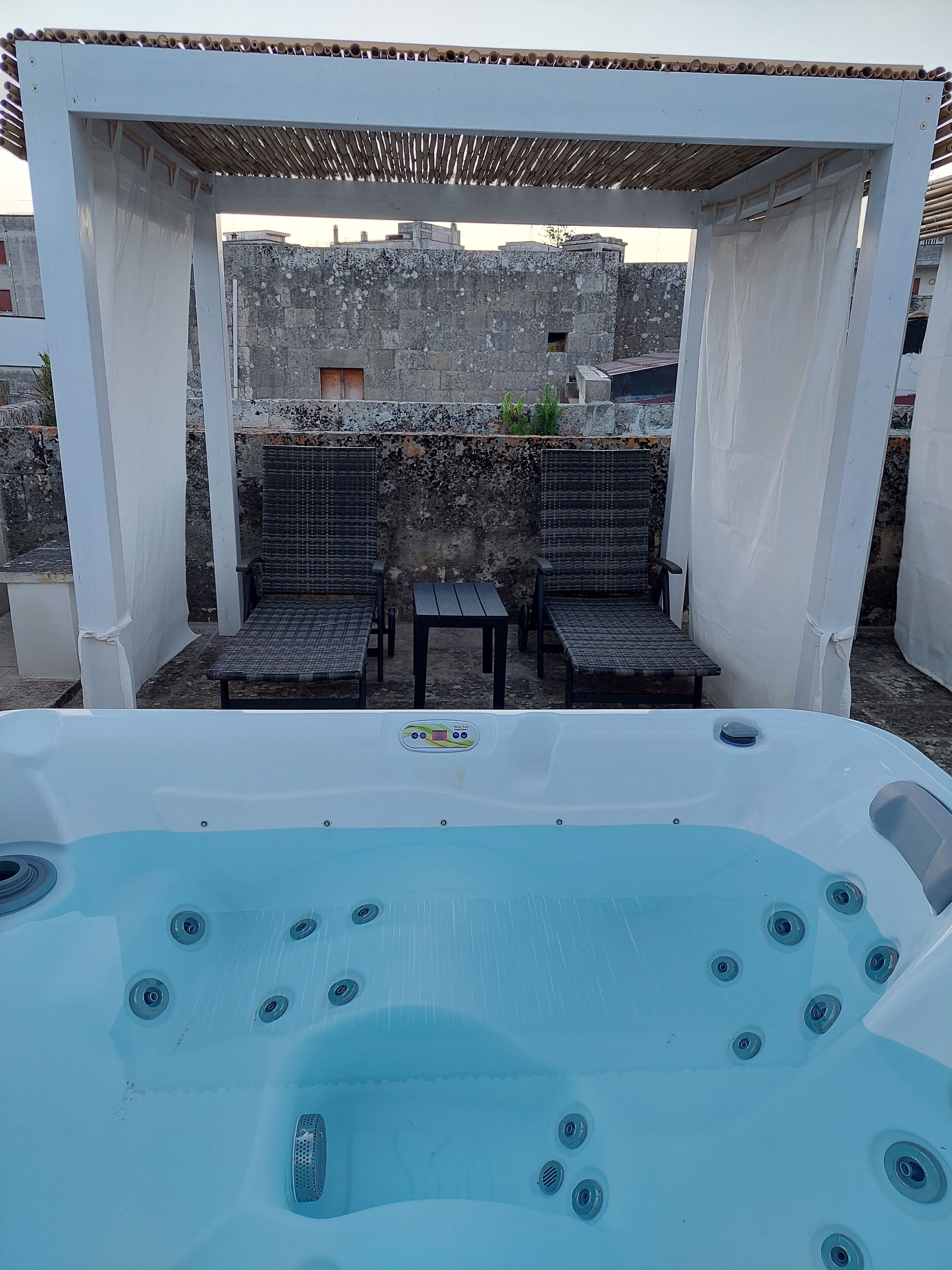 Eine Dachterrasse mit Whirlpool, Sitzgelegenheit und einer Wand aus Stein.
