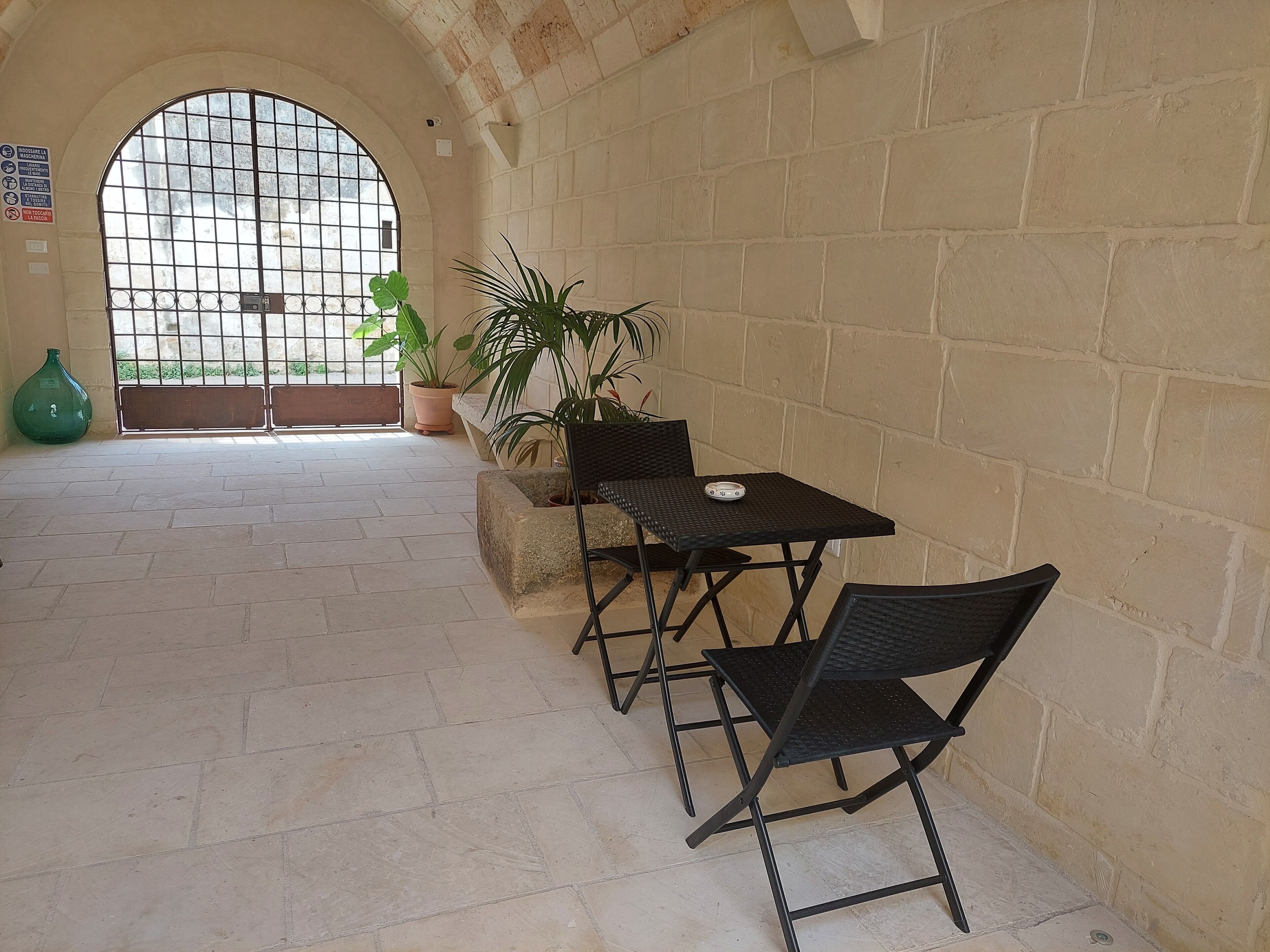 A corridor with a tiled floor, a potted plant, a green vase, and a metal gate with a view outside.